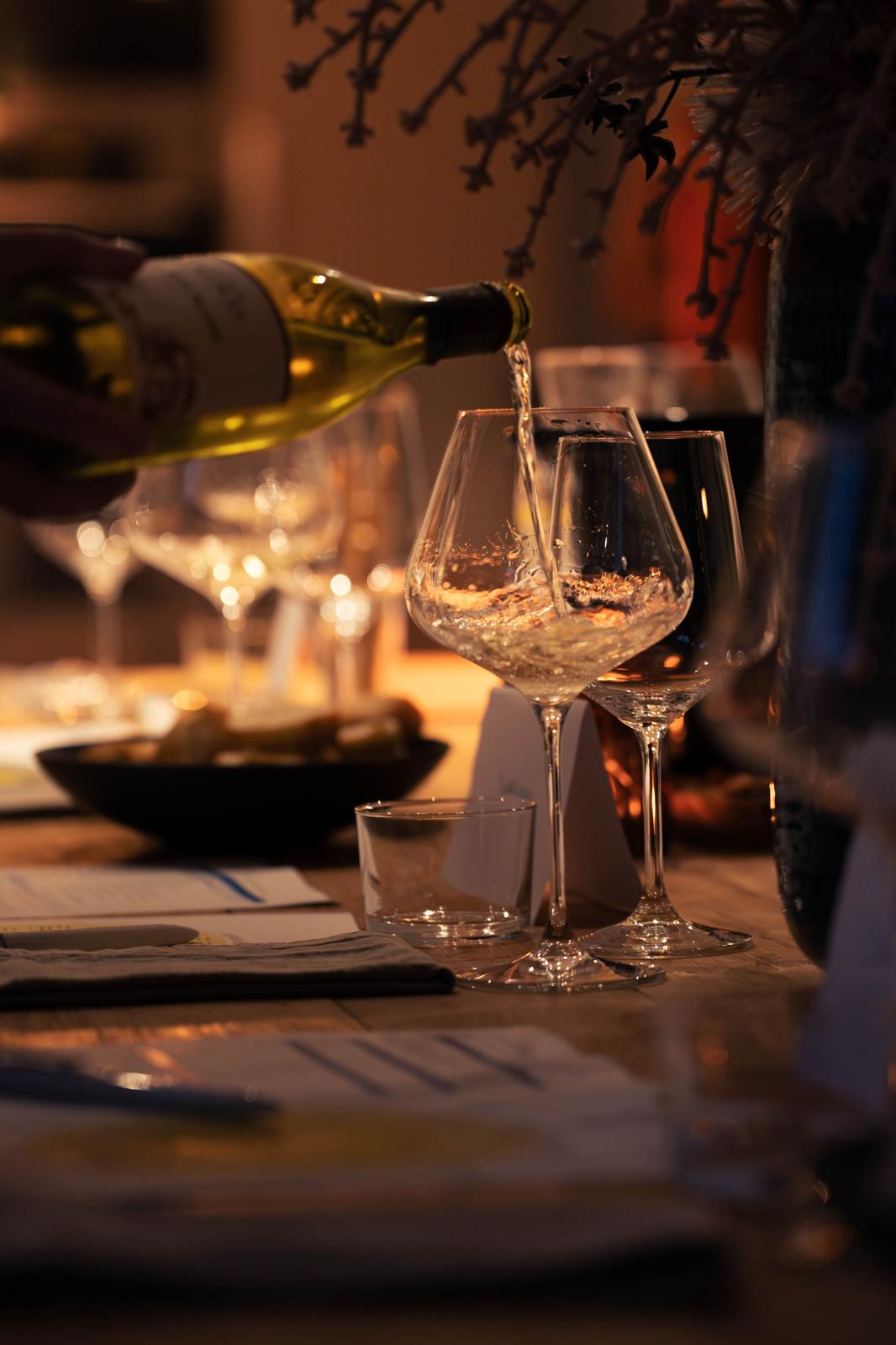 Witte wijn wordt ingeschonken naast glazen en een schaal hapjes